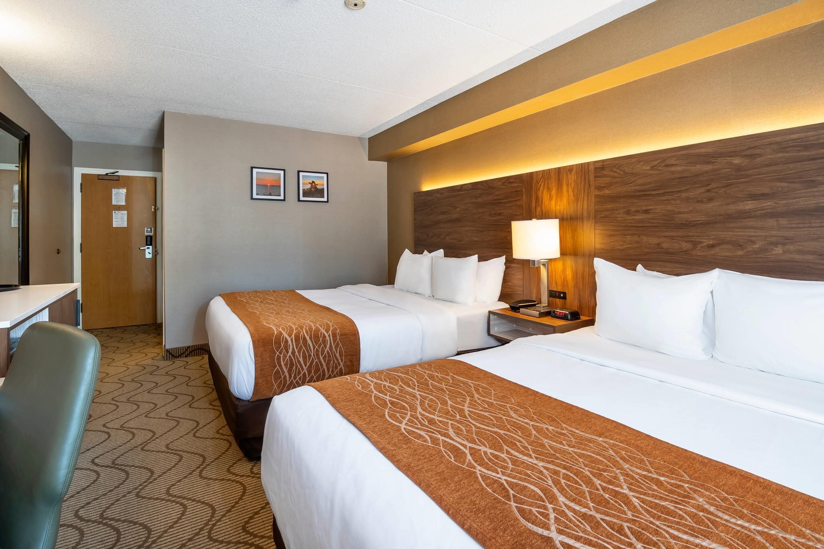 Une chambre d’hôtel avec deux lits, un bureau, une chaise, une table de chevet avec une lampe et une horloge fixée au mur.
