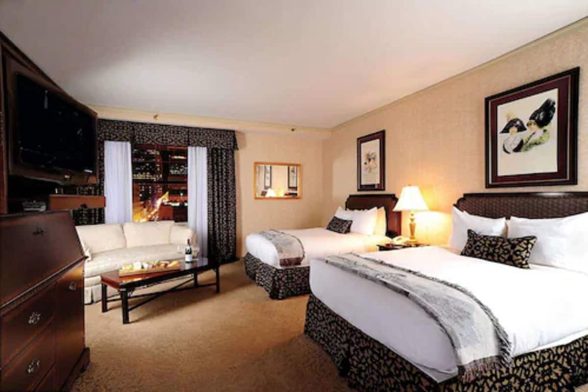 A hotel room with a sofa, two beds, a TV, a bookshelf, and a framed picture on the wall.