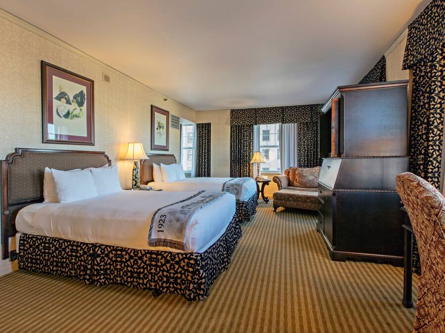 A hotel room with two beds, a desk, a chair, and a large mirror.