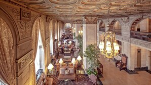 Un vaste hall d’entrée avec un plafond richement décoré, plusieurs espaces aménagés pour s’asseoir et un escalier.