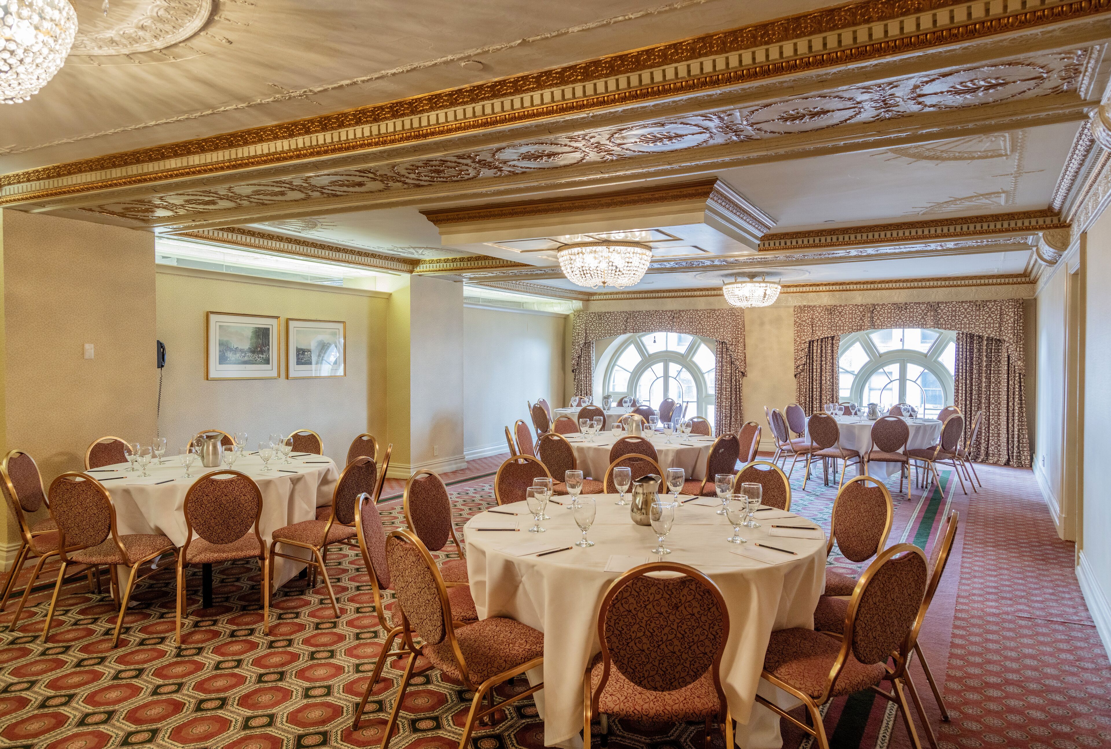 A banquet hall with round tables, chairs, and chandeliers.
