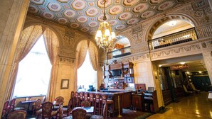 Une vaste salle à manger, ornée d’un plafond richement décoré, de lustres et d’un bar dont l’enseigne indique « Bar à cigares ».