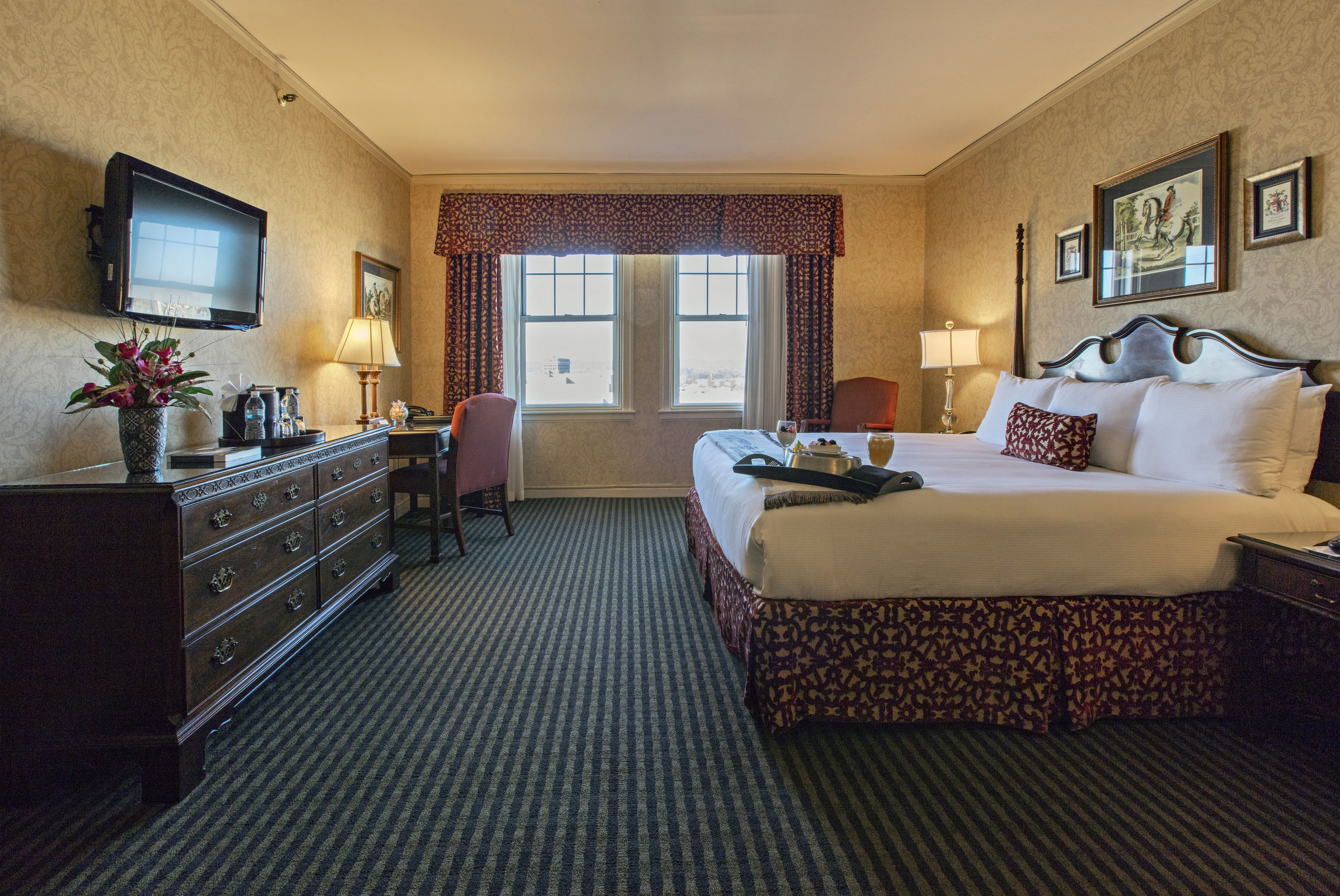 Ein Hotelzimmer mit Bett, Kommode, Schreibtisch, Stuhl, Fernseher und Fenstern.