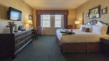 A hotel room with a bed, dresser, desk, chair, television, and windows.