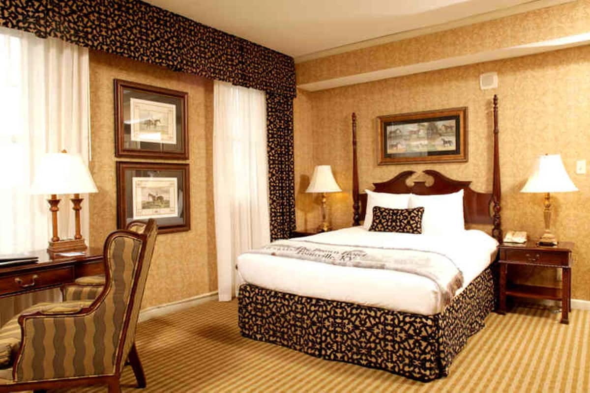 A hotel room with a large bed, two bedside tables with lamps, a chair, and framed pictures on the walls.