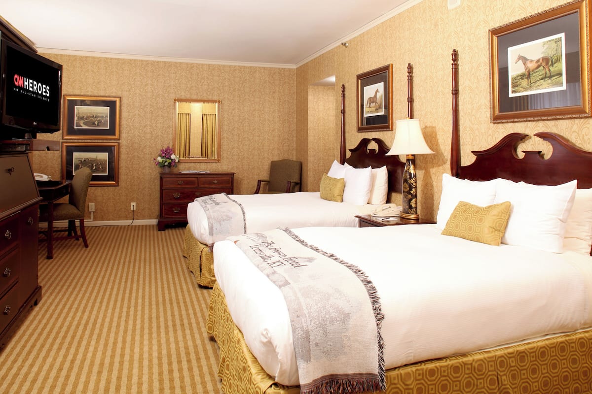 A hotel room with two beds, a television, a desk, and a chair.