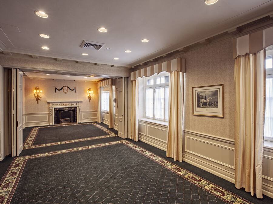 A spacious hotel lobby with a patterned carpet, a fireplace, and large windows with curtains.