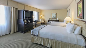 A hotel room with two beds, a desk with a television, and a chair.