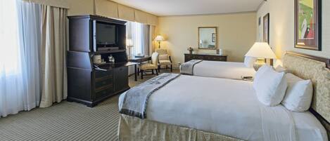 Une chambre d’hôtel avec deux lits, un bureau avec une télévision et une chaise.