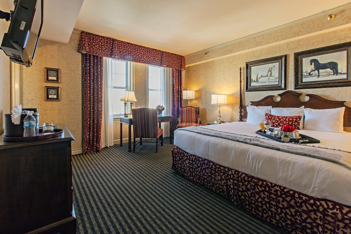 A hotel room with a large bed, a desk with a chair, a TV, and framed pictures on the wall.