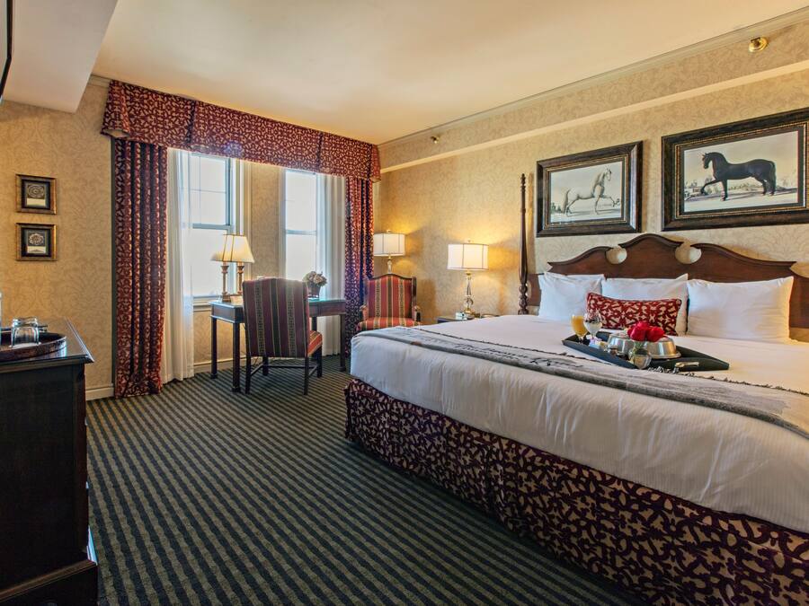 Een hotelkamer met een groot bed, een bureau met stoel, een televisie en ingelijste foto's aan de muur.