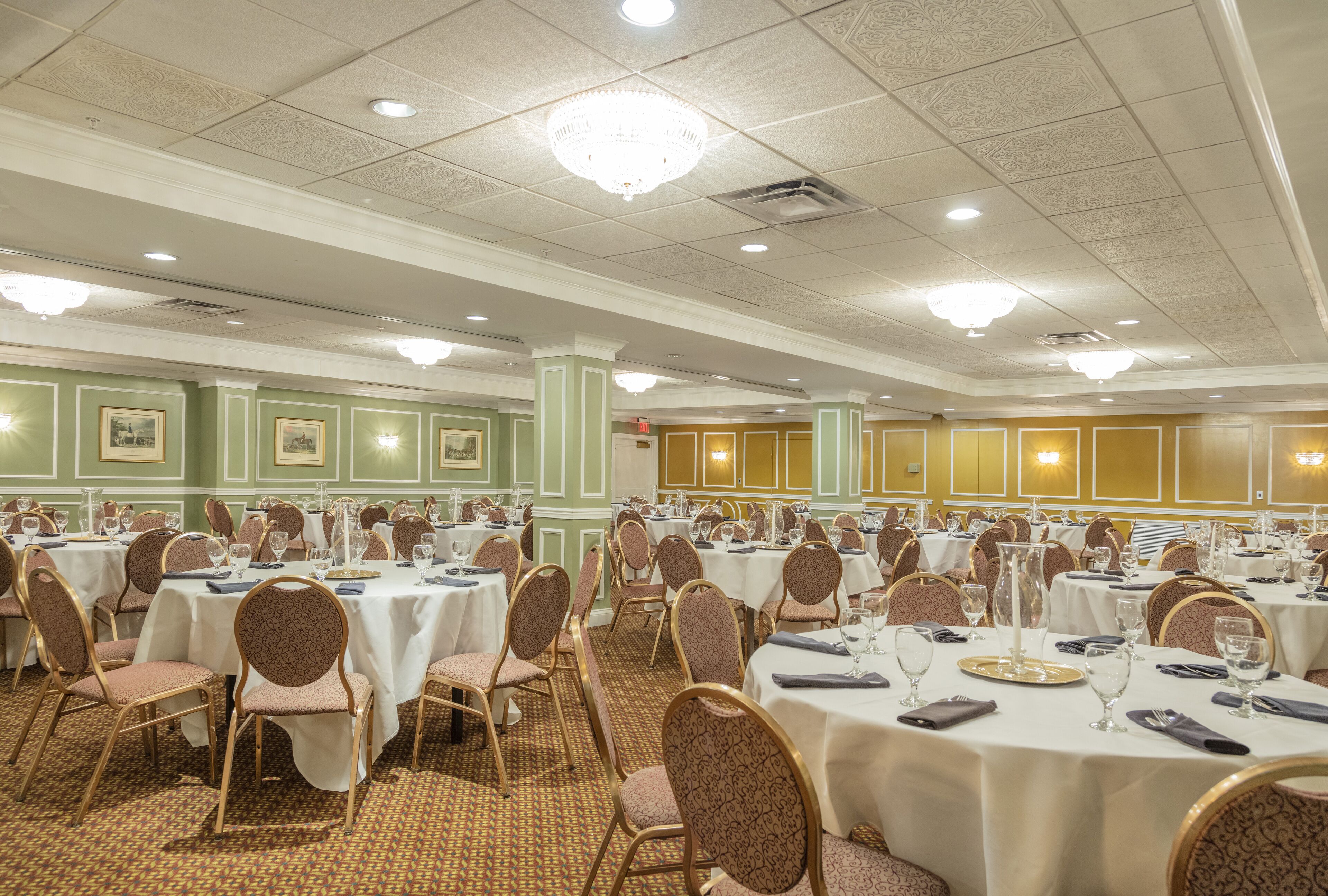 A banquet hall with multiple round tables, each set with chairs, plates, and cutlery.