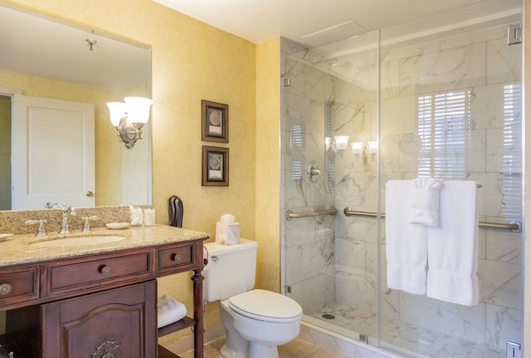 A bathroom with a marble shower, a sink with a vanity, and a toilet.