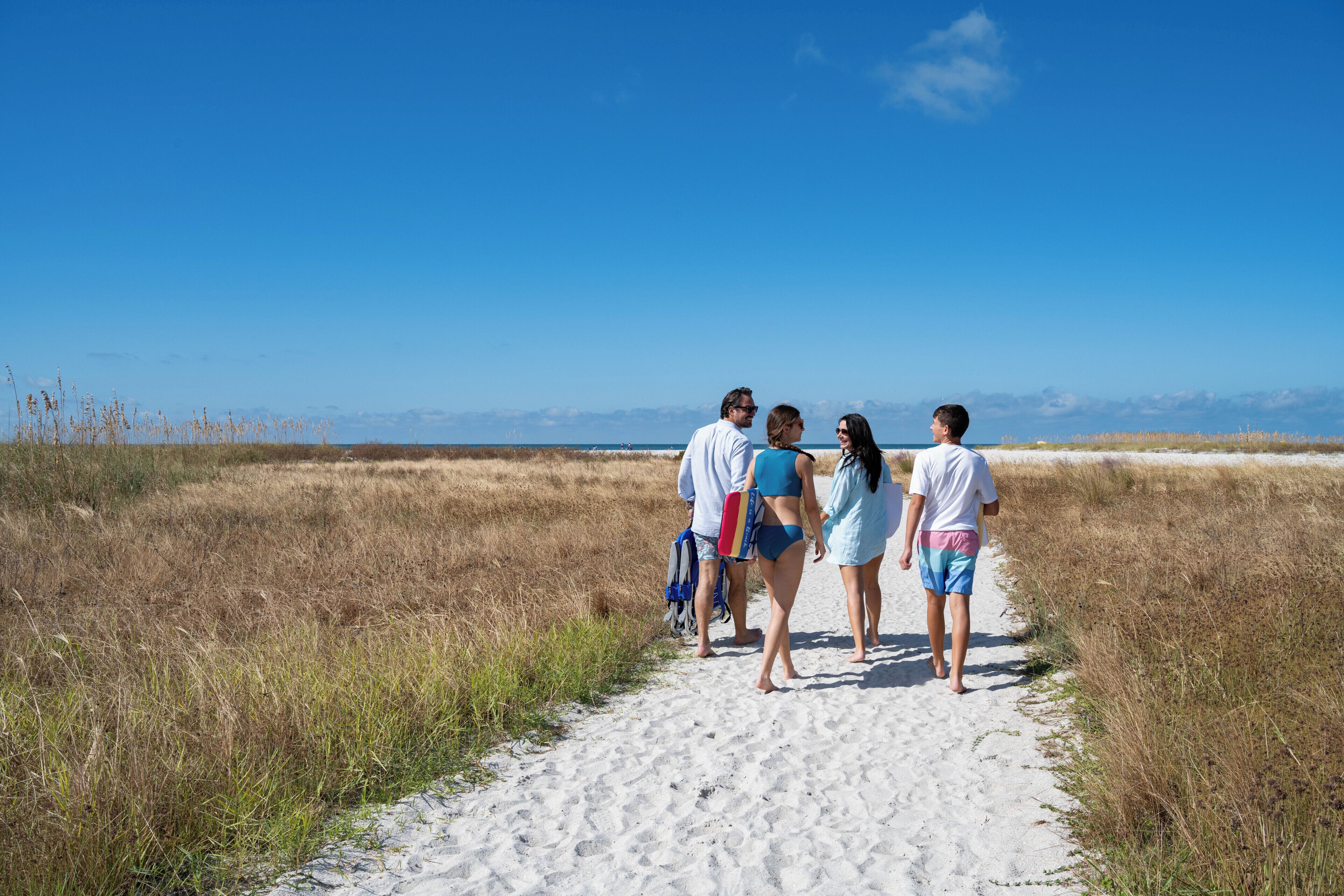 A group of people walking on a sandy path with a clear sky and distant horizon.