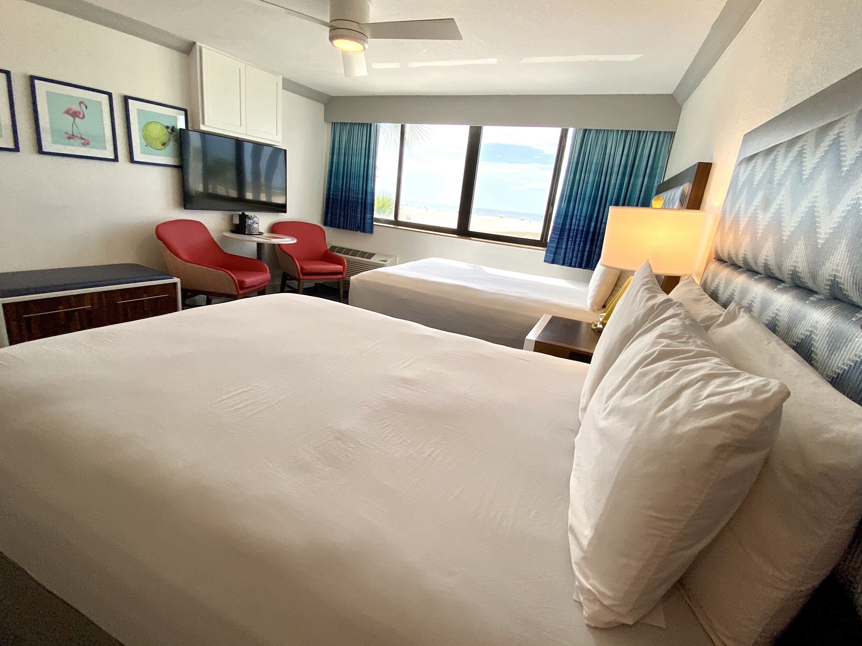 A hotel room with a large bed, a desk with a chair, a TV, and a window with curtains.