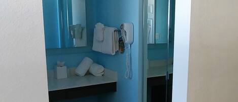 A bathroom with a blue wall, a white sink, a hairdryer, and a mirror.