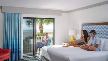 Een hotelkamer met een bed, een rode stoel, een balkon met uitzicht op het strand en een groot raam.