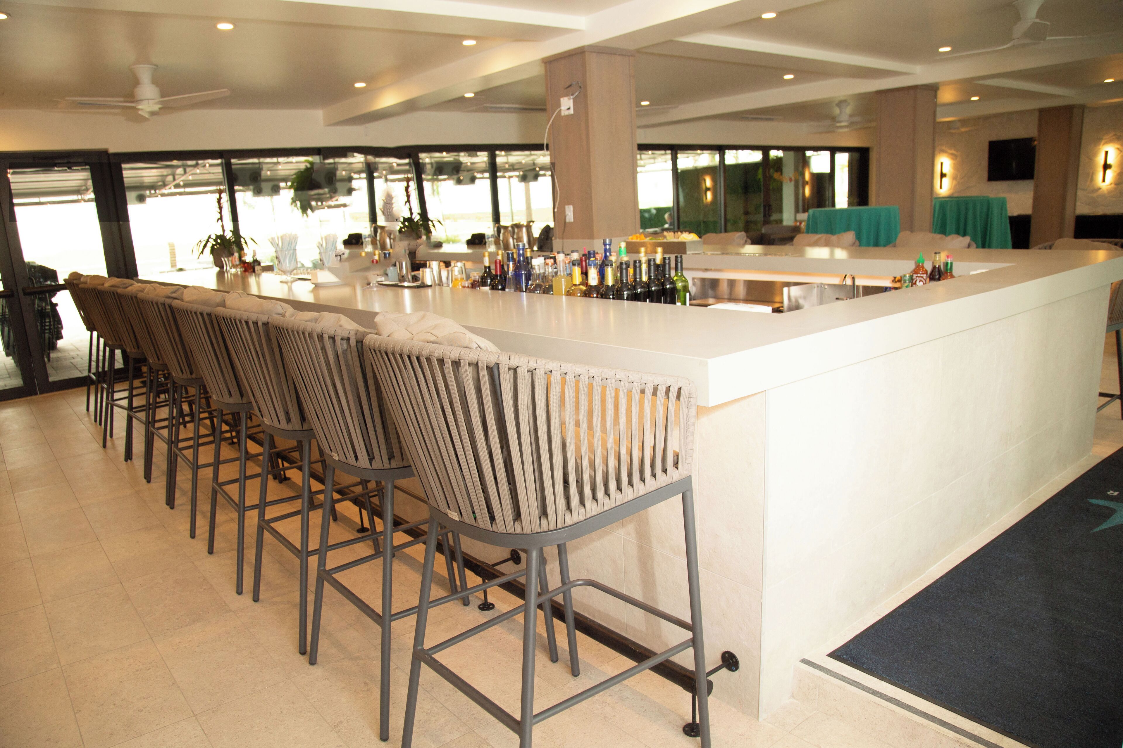 A bar area with a long counter, multiple bar stools, and a variety of bottles.