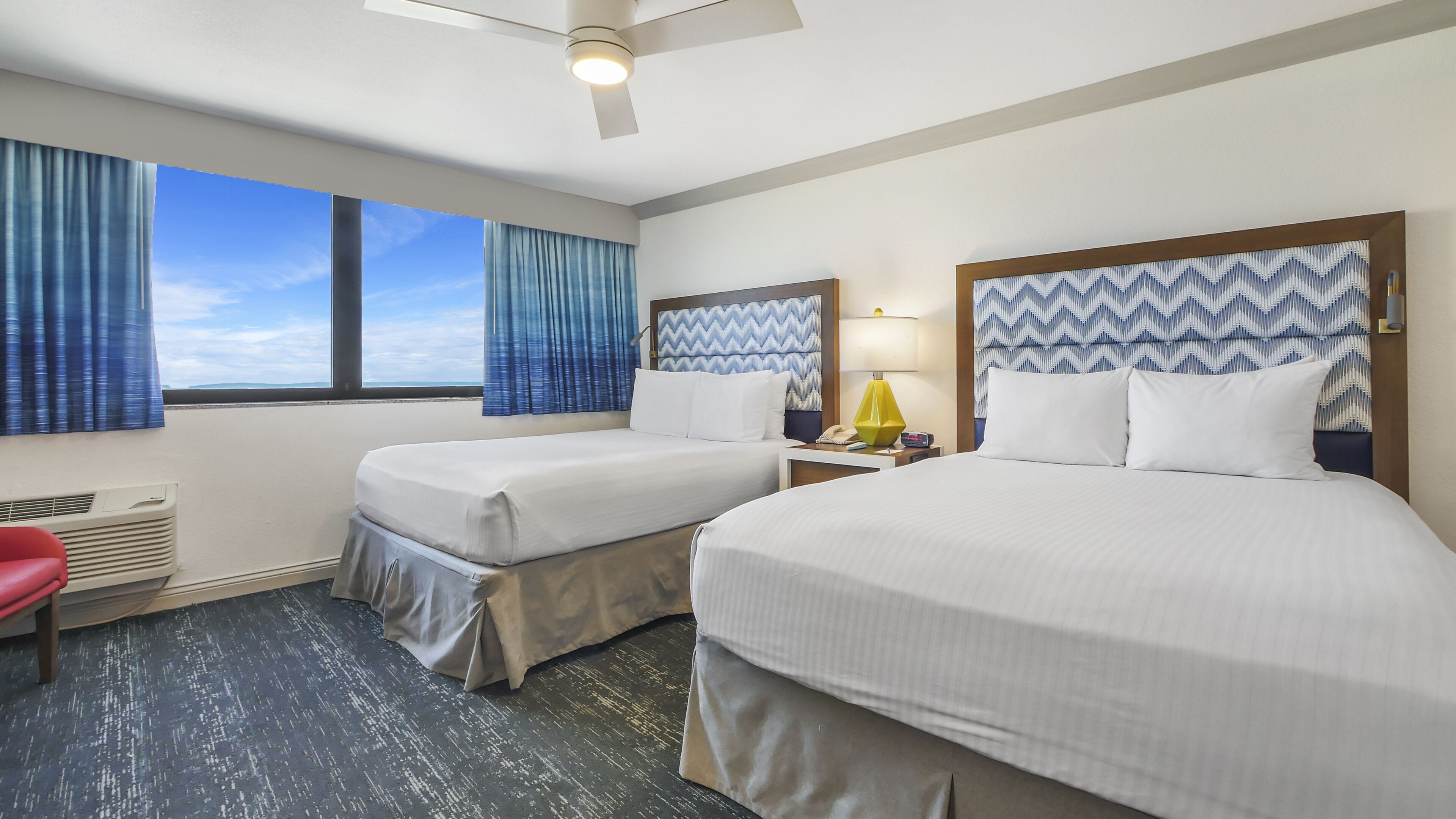 A hotel room with two beds, a desk, a chair, and a window with curtains.
