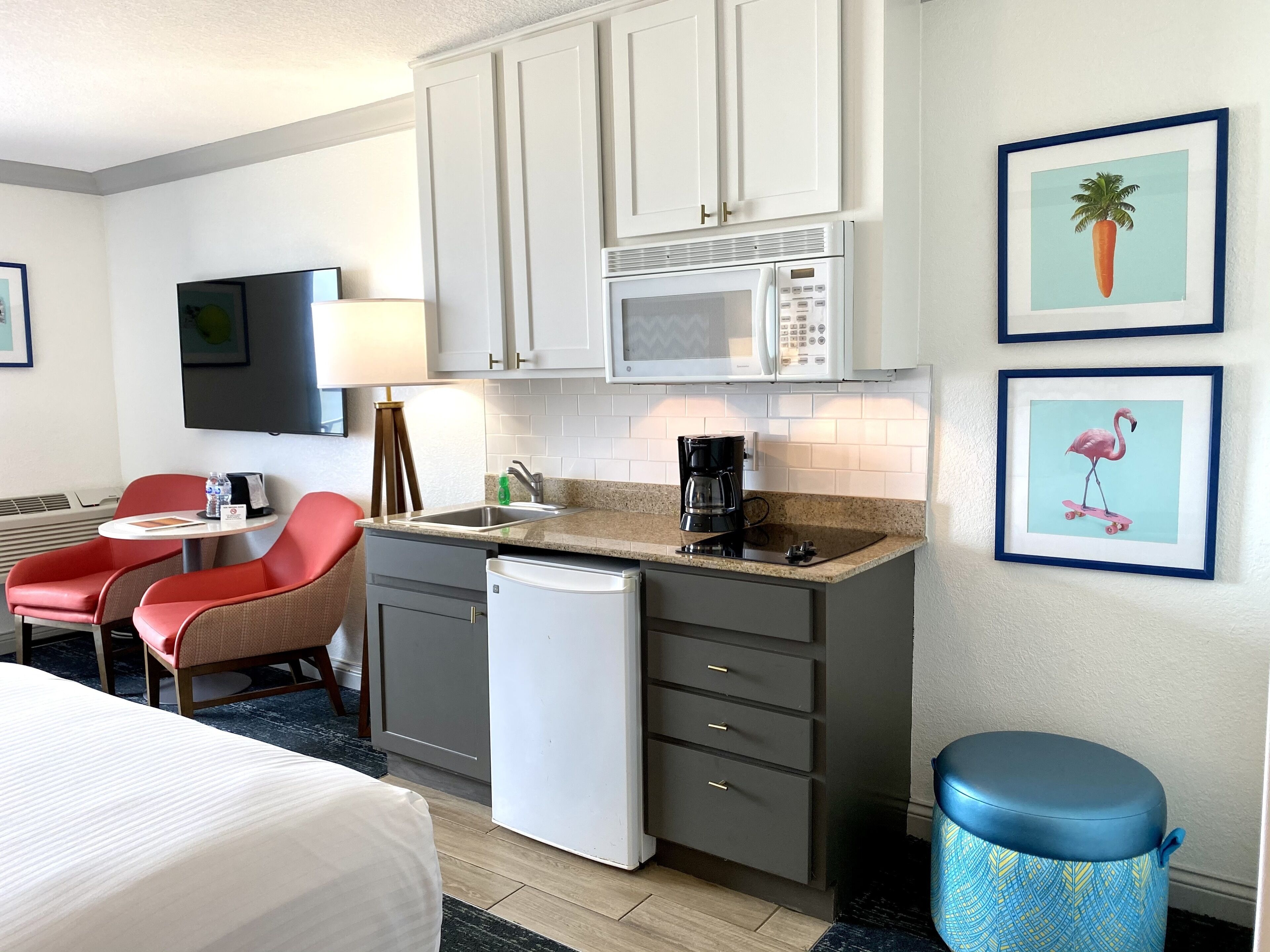 Une chambre d’hôtel compacte comprenant un coin cuisine, un lit, un petit espace repas et une poubelle.