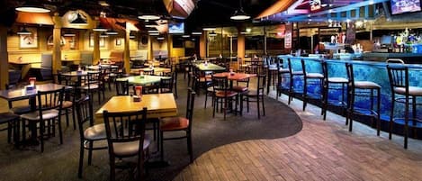 Un restaurante con varias mesas y sillas, una zona de bar con mostrador y una mesa de billar.