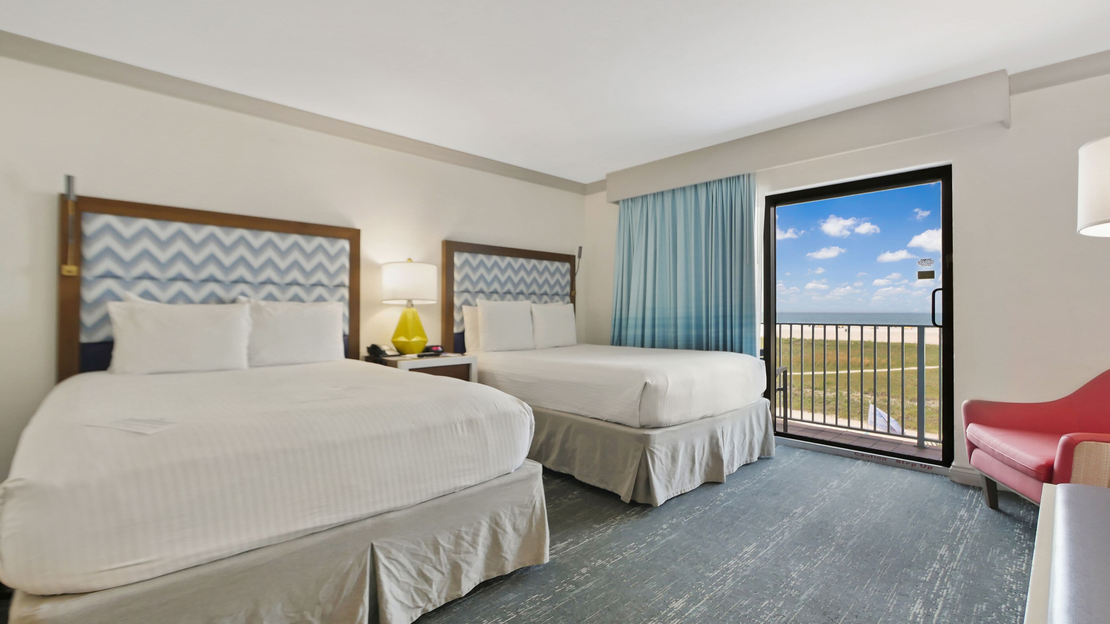 Habitación de hotel con dos camas, un balcón con vistas y una silla roja.