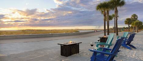 A beachside lounge with a fire pit, lounge chairs, and palm trees.