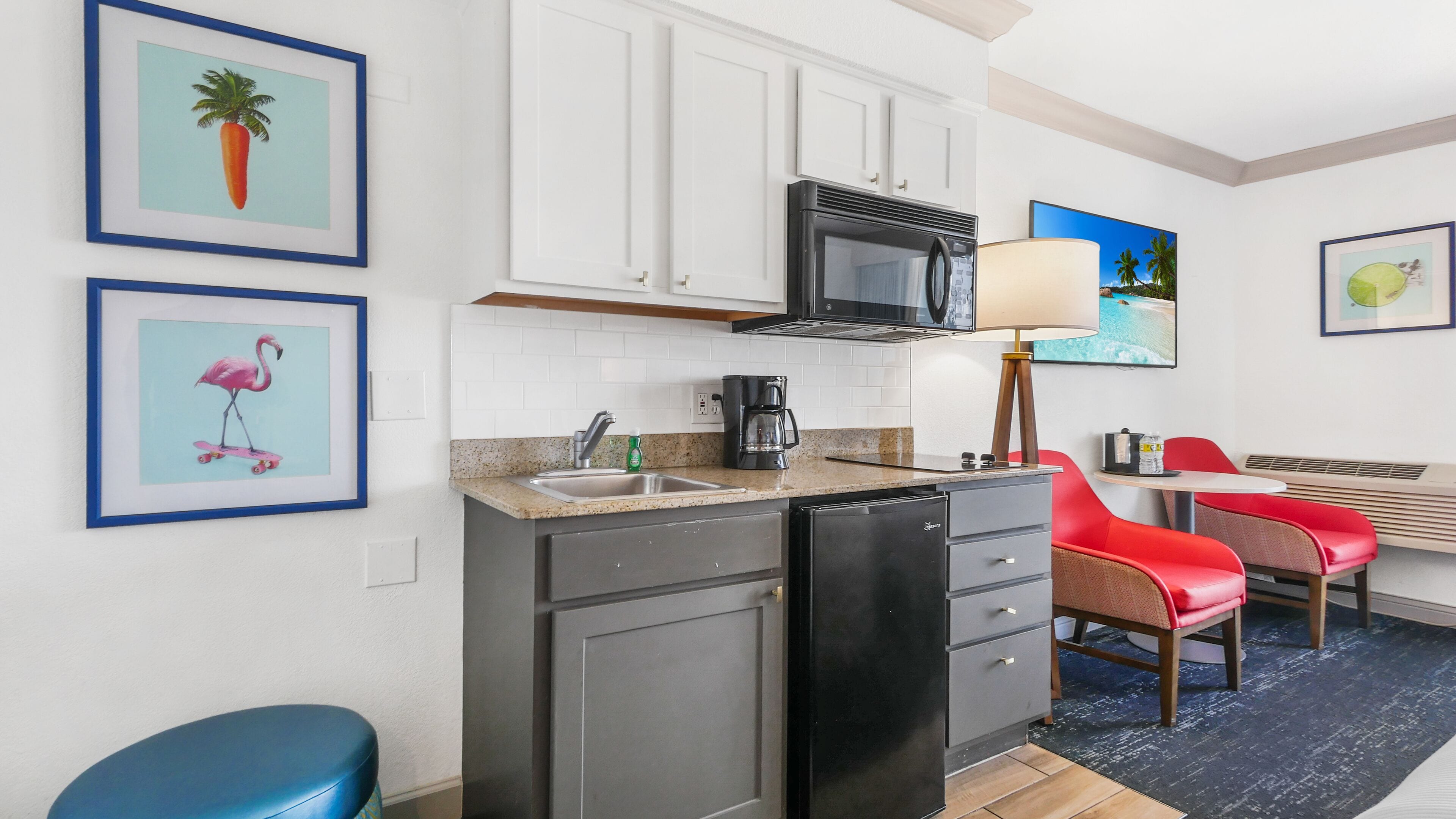 A compact kitchen with a microwave, coffee maker, and a small refrigerator. There are two chairs and a table in the adjacent dining area.