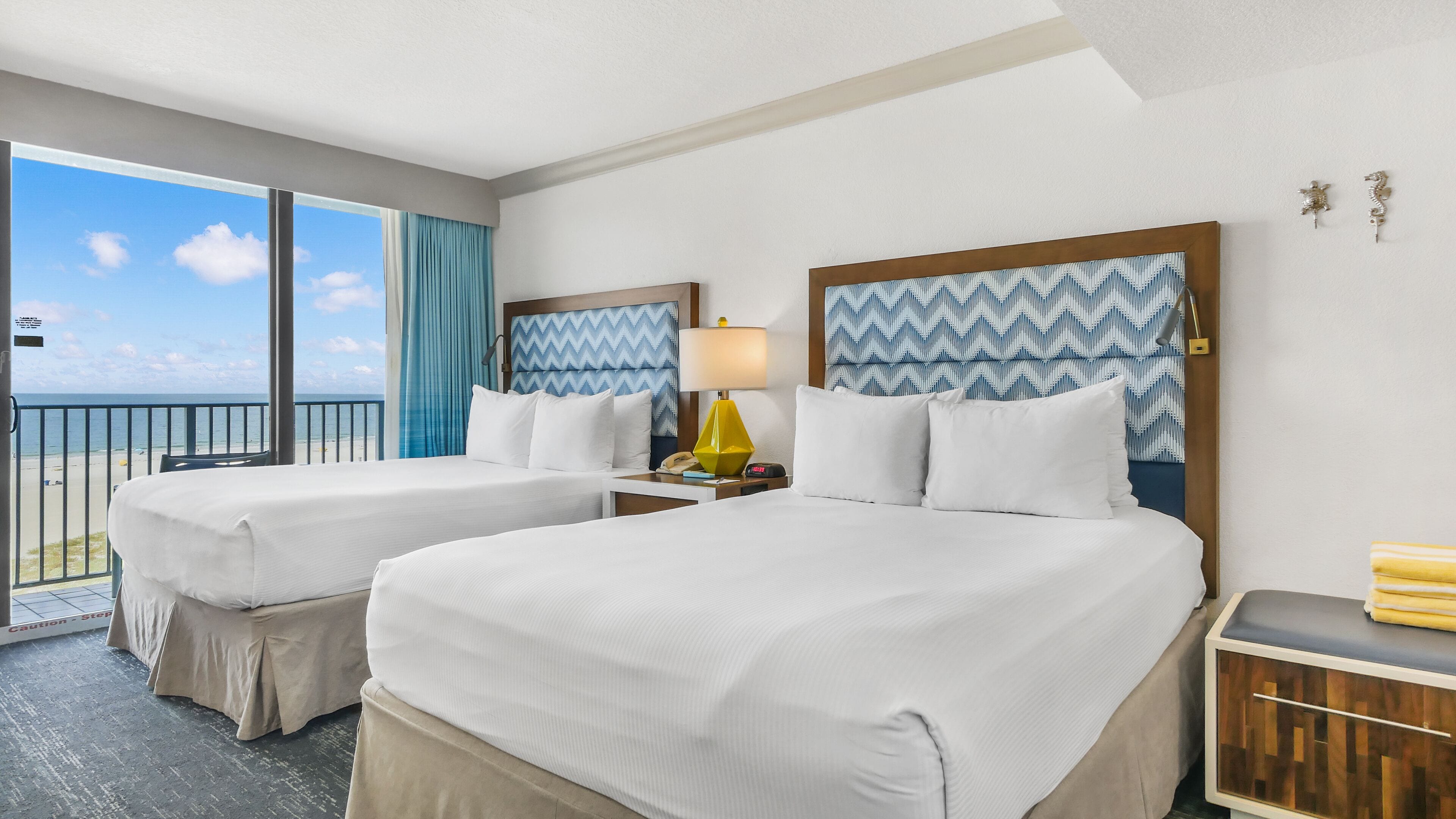 Habitación de hotel con dos camas, vista a la playa y un ventanal con cortinas.