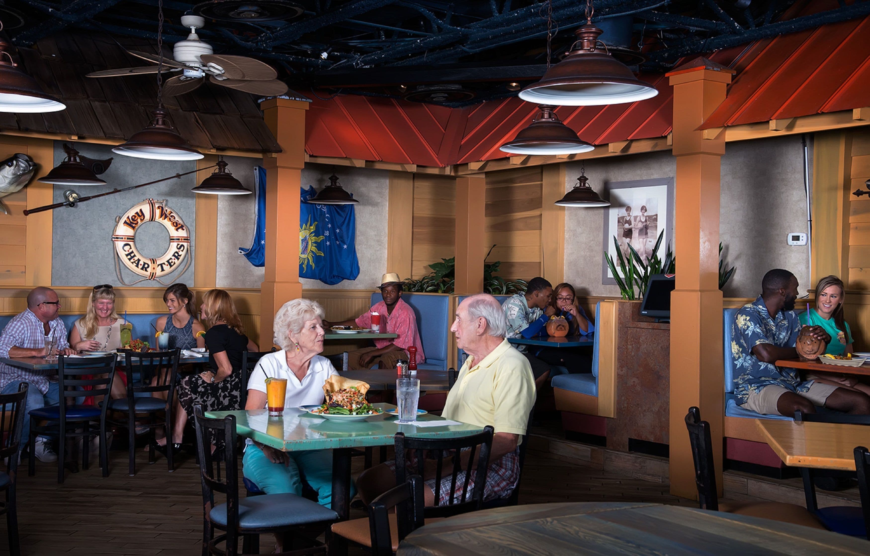 A restaurant interior with booths and tables, ceiling fans, and wall decorations including a flag and a circular sign.