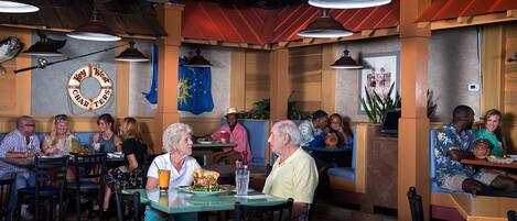 A restaurant interior with booths and tables, ceiling fans, and wall decorations including a flag and a circular sign.