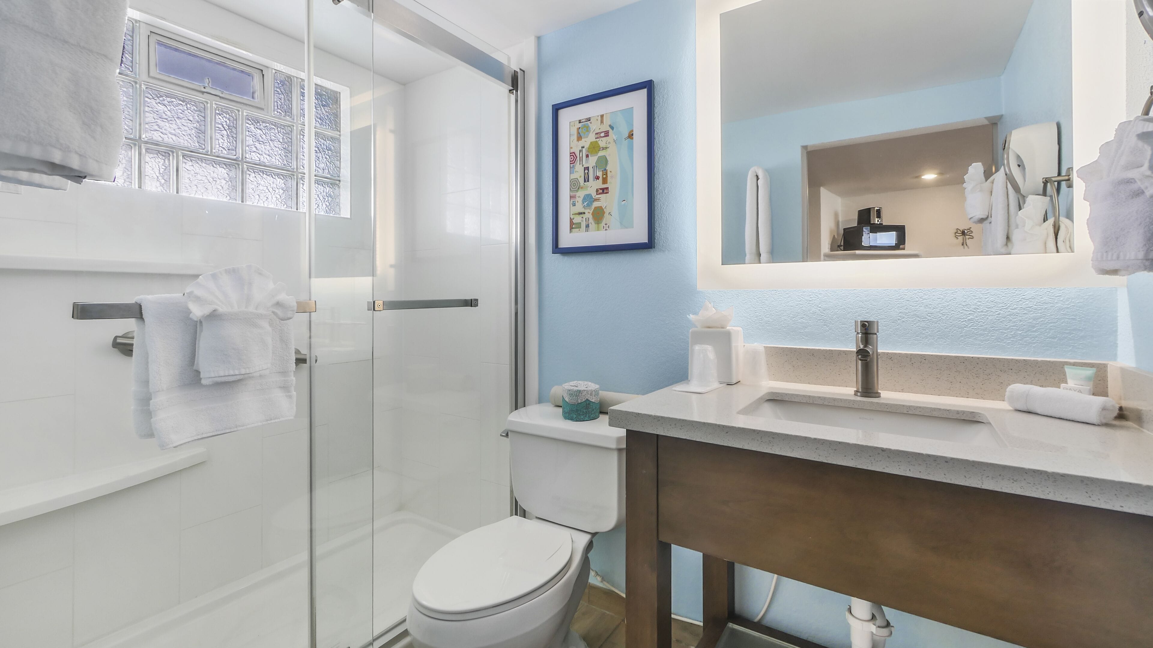 Un baño moderno con cabina de ducha de vidrio, inodoro, lavabo con espejo y toallero.