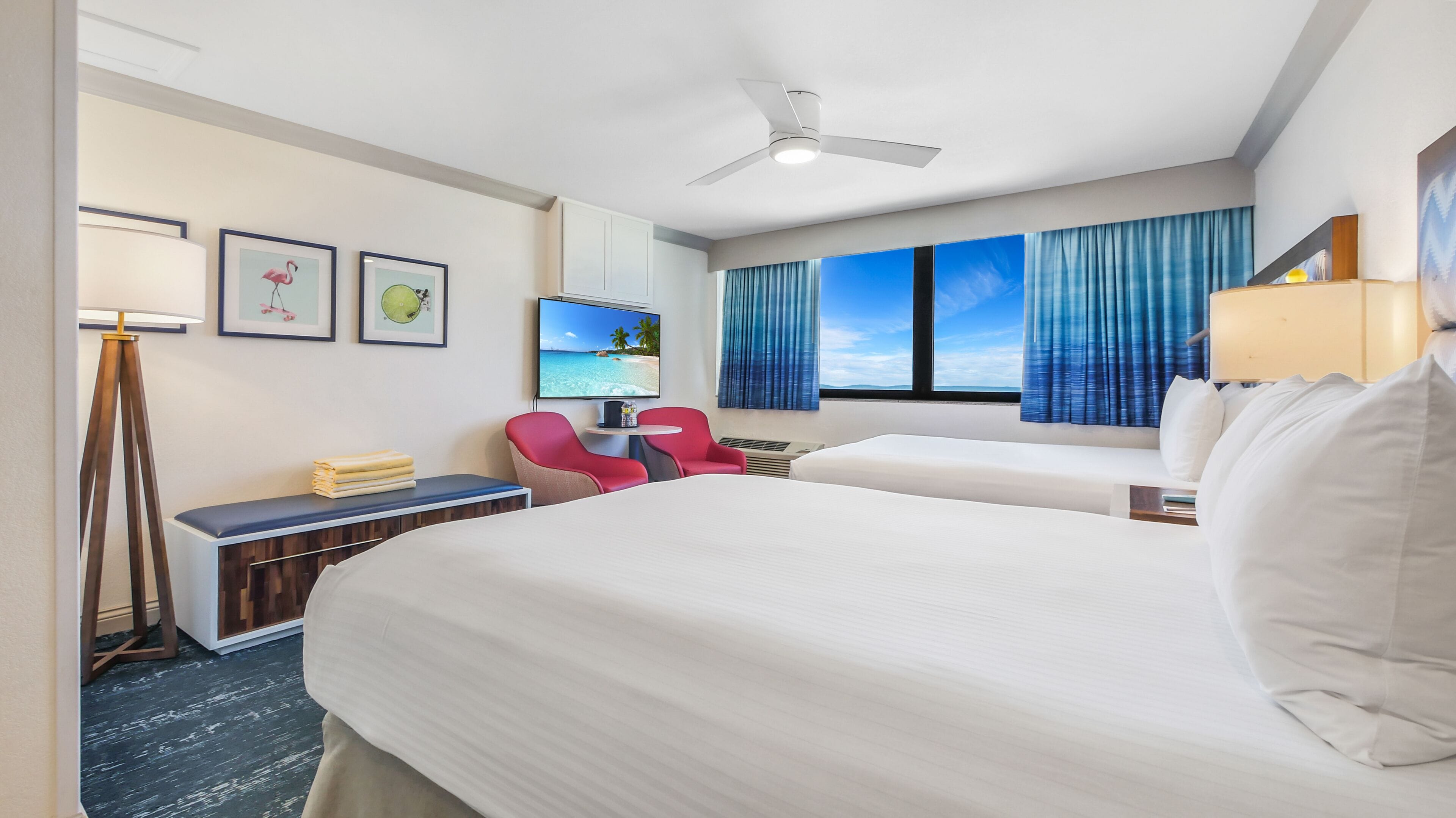 Een hotelkamer met twee bedden, een bureau, een stoel, een televisie en een plafondventilator.