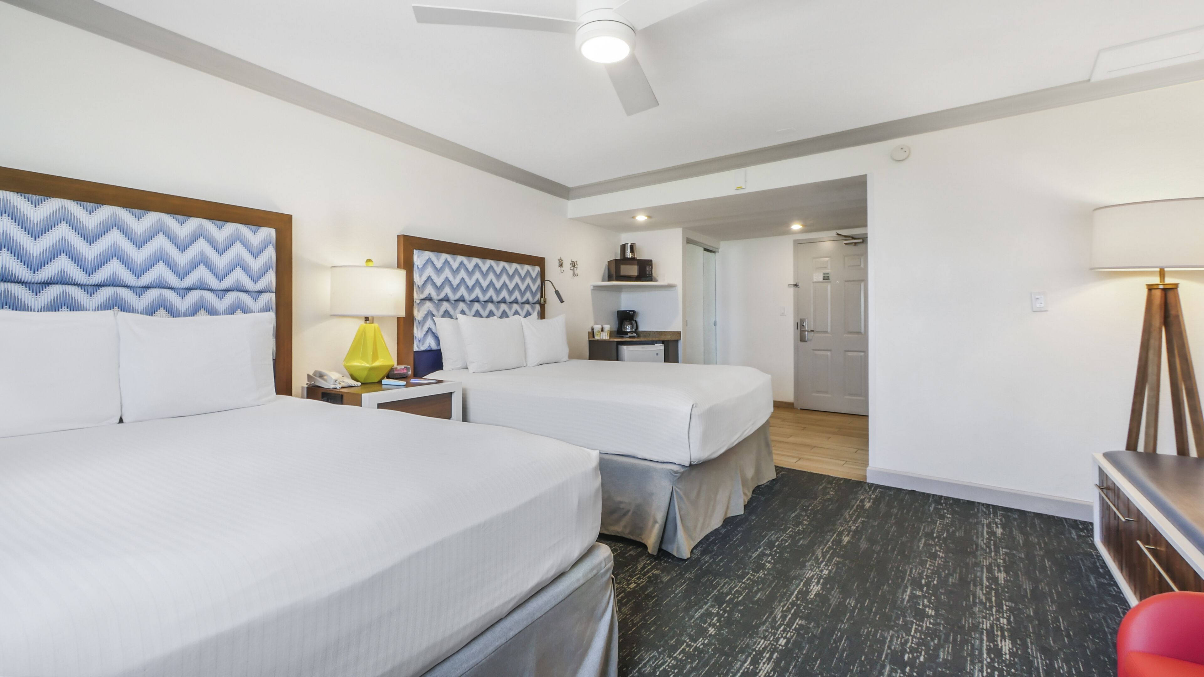 Een hotelkamer met twee bedden, een bureau, een lamp, een magnetron en een deur naar een andere kamer.