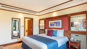 Habitación de hotel con una cama grande, una mesita de noche con lámpara, un espejo y un cuadro en la pared.