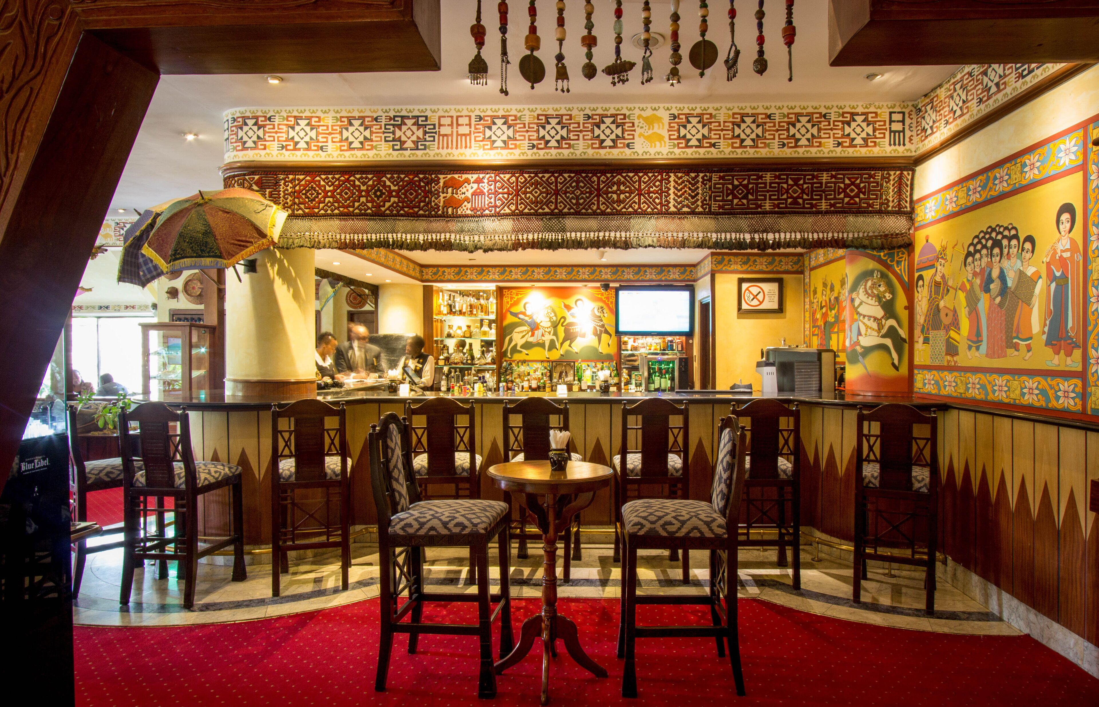 A bar area with wooden chairs, a round table, and a patterned wall.