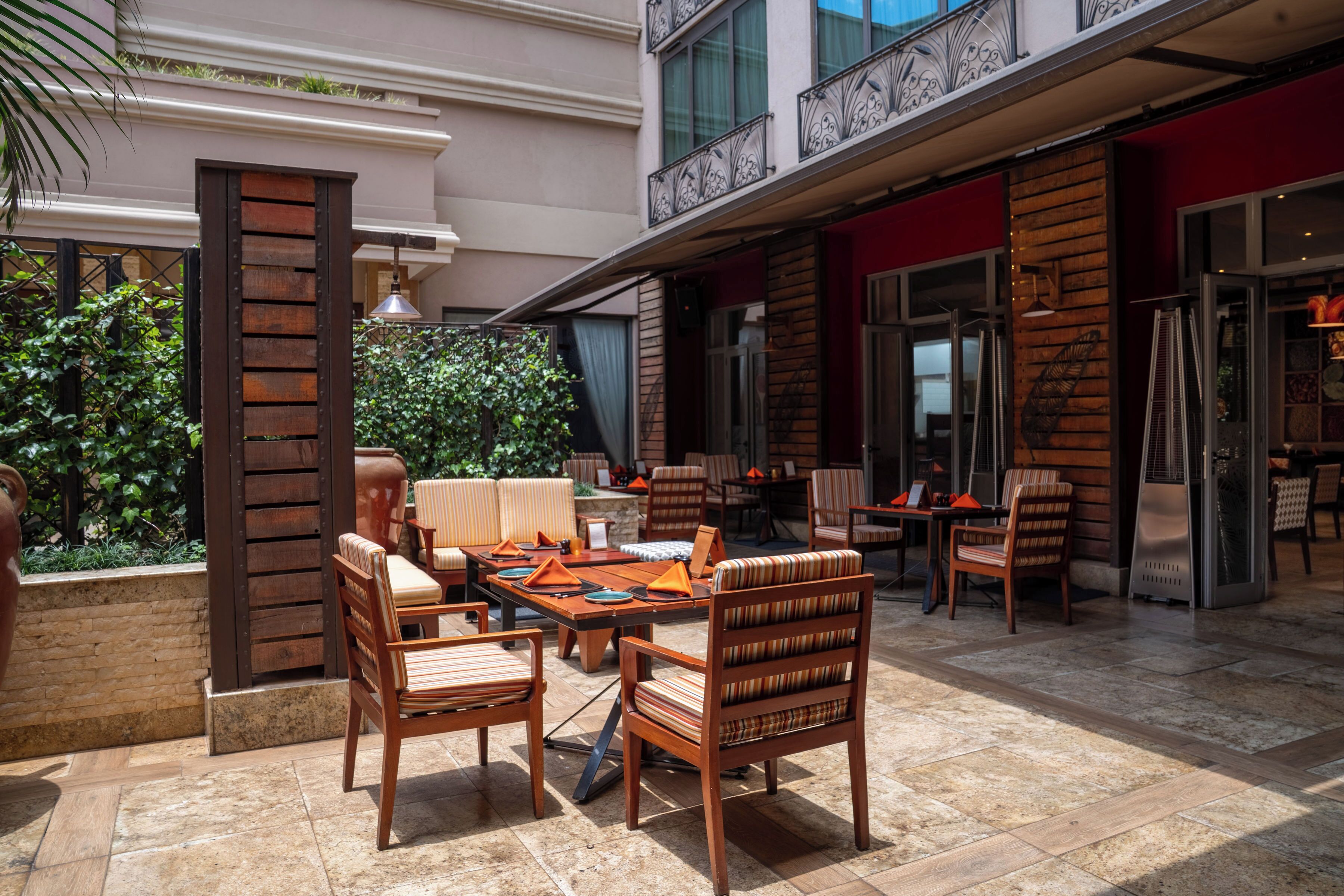 An outdoor patio area with wooden furniture, a brick wall, and a view of the building's exterior.
