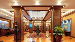 A lobby with wooden pillars, a central statue, a chandelier, and a reception desk. - Nairobi Serena Hotel (Nairobi)
