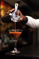 Un barman sirviendo una bebida en una copa de martini.