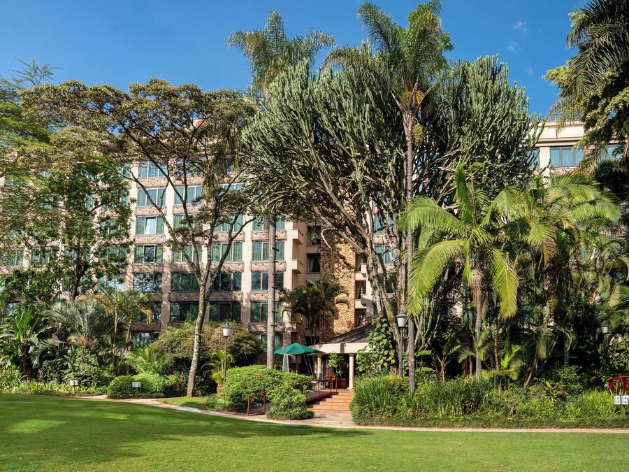 Un hotel con un jardín exuberante, una zona de estar cubierta y un puente rojo.