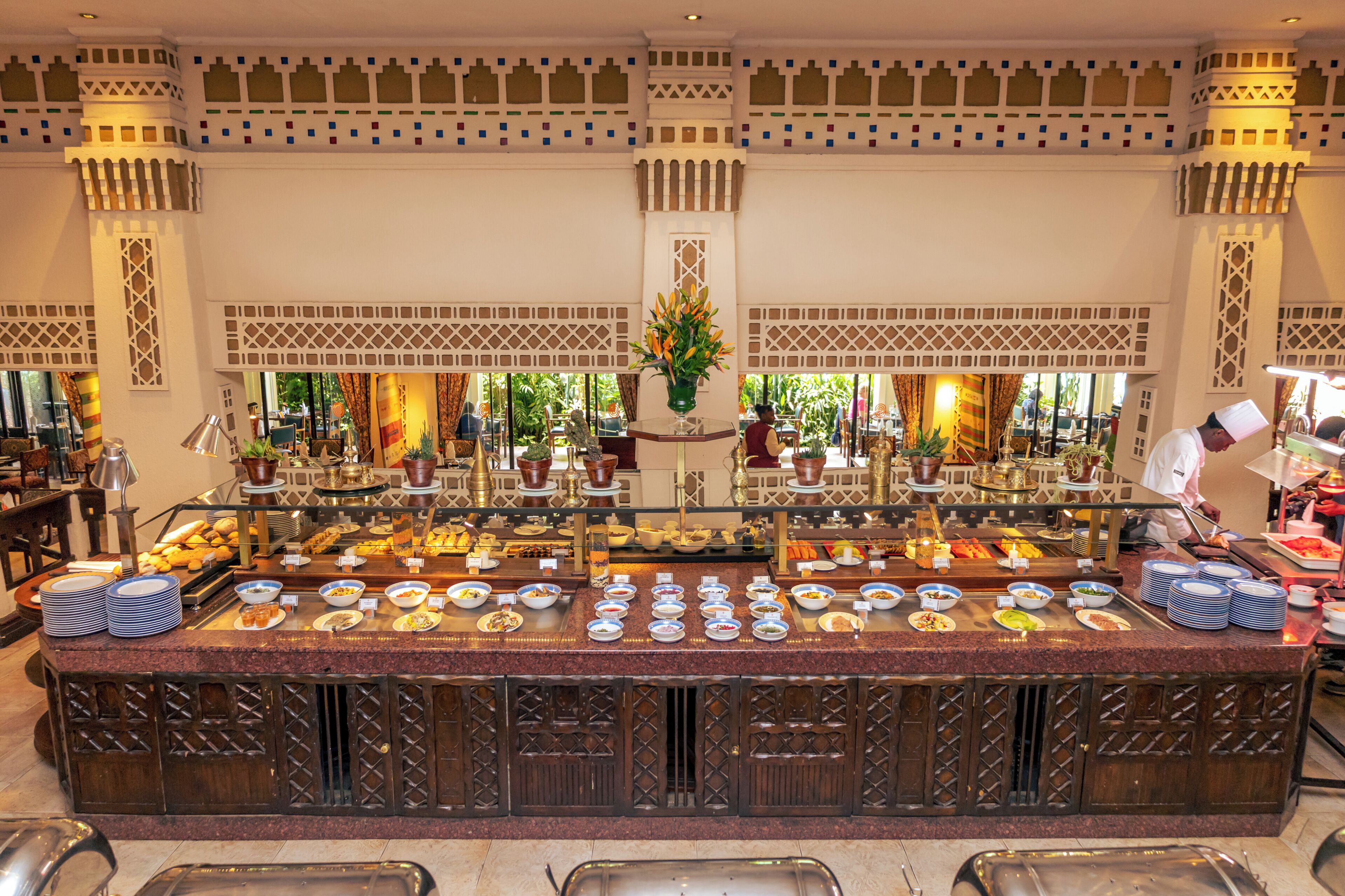 A buffet with a variety of dishes, a central decorative plant, and a patterned ceiling.