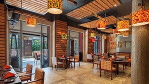 A restaurant with wooden walls, large windows, and hanging lamps. Tables are set with orange napkins and chairs. - Nairobi Serena Hotel (Nairobi)