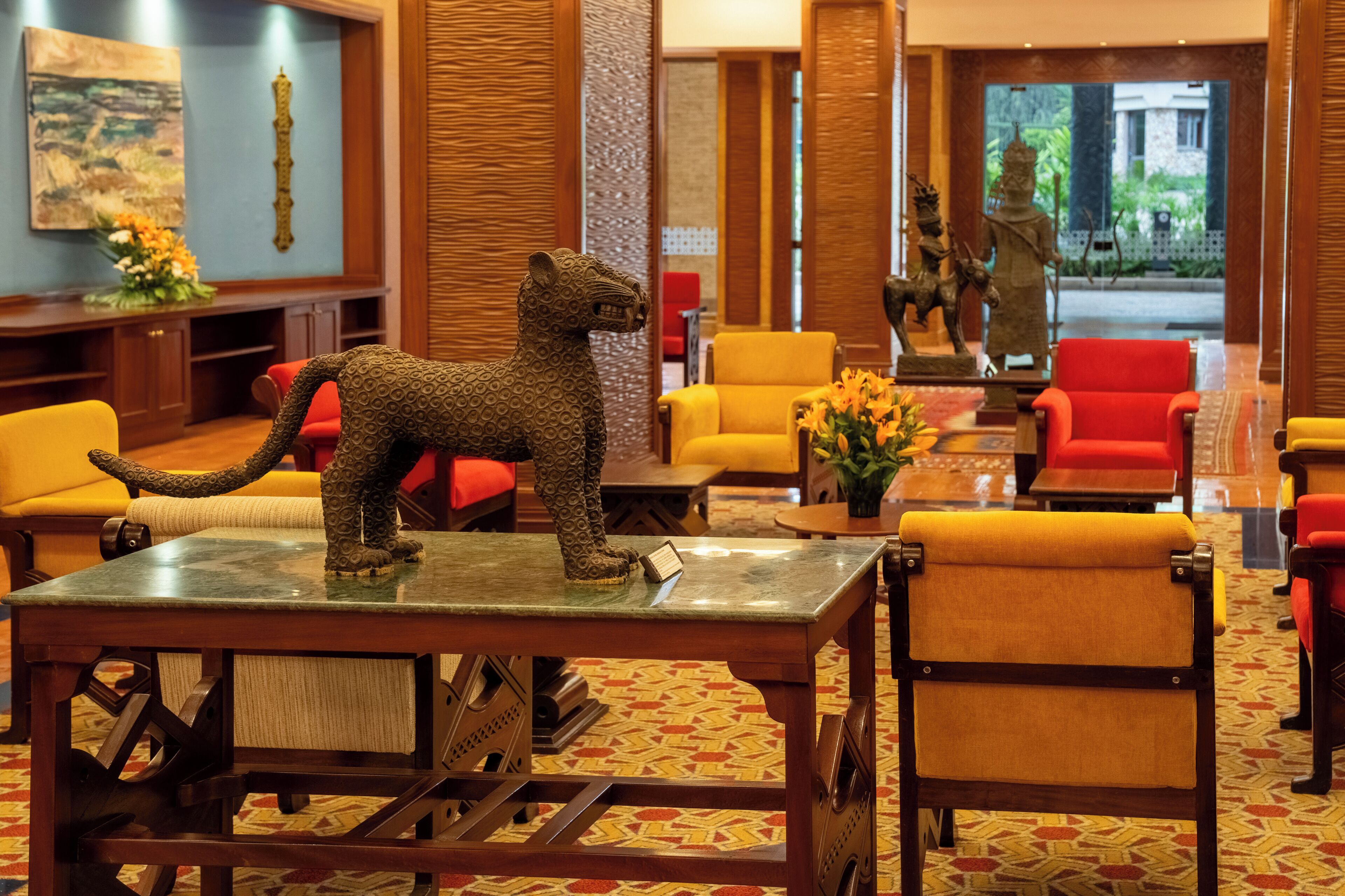 A lobby with a lion statue on a table, red and yellow chairs, and a wooden reception desk.