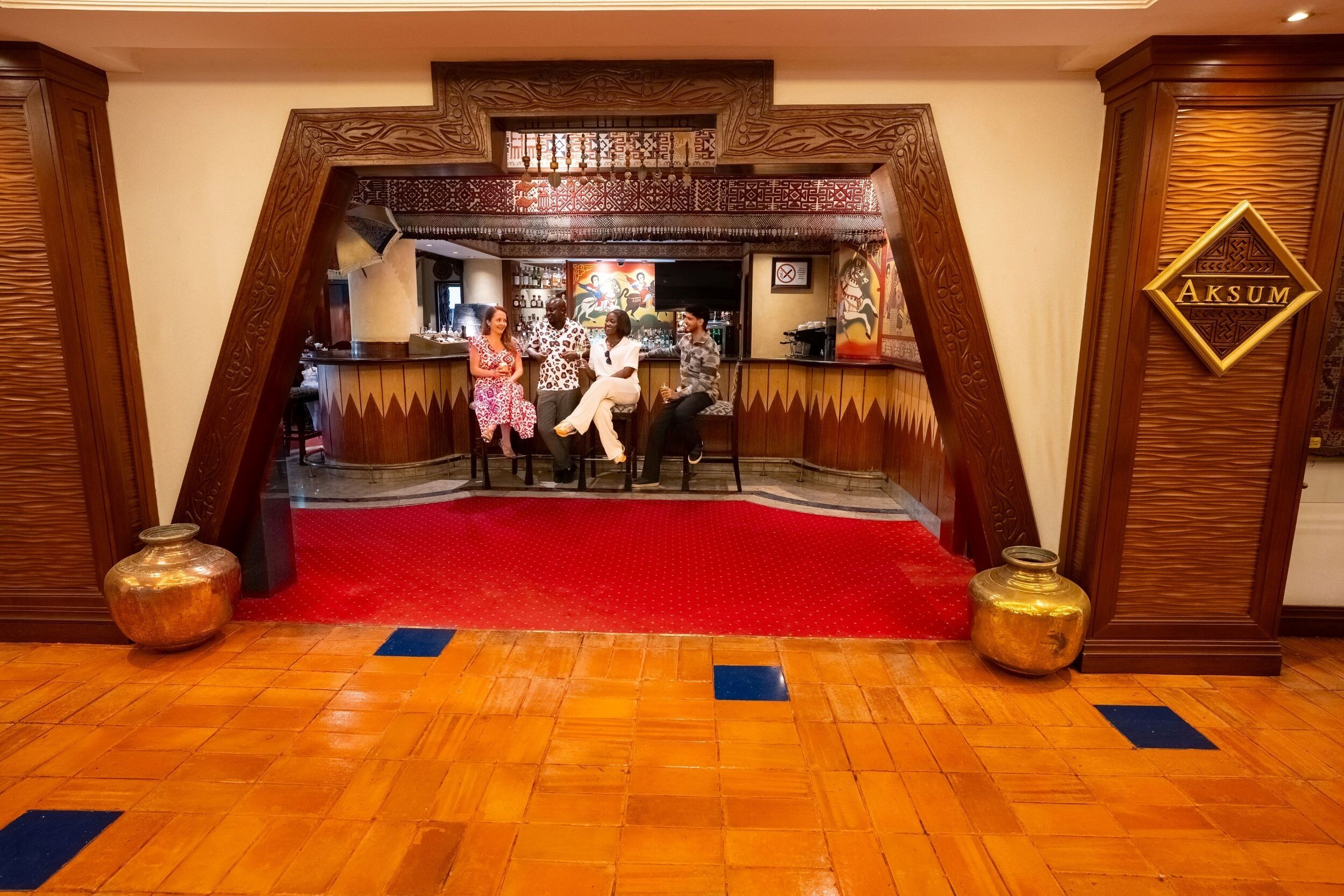Un espace bar avec un tapis rouge, une décoration en bois et une enseigne indiquant « AKSUM ».