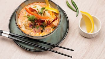 A bowl of soup with vegetables and herbs, a pair of chopsticks, and a small bowl with lemon slices.