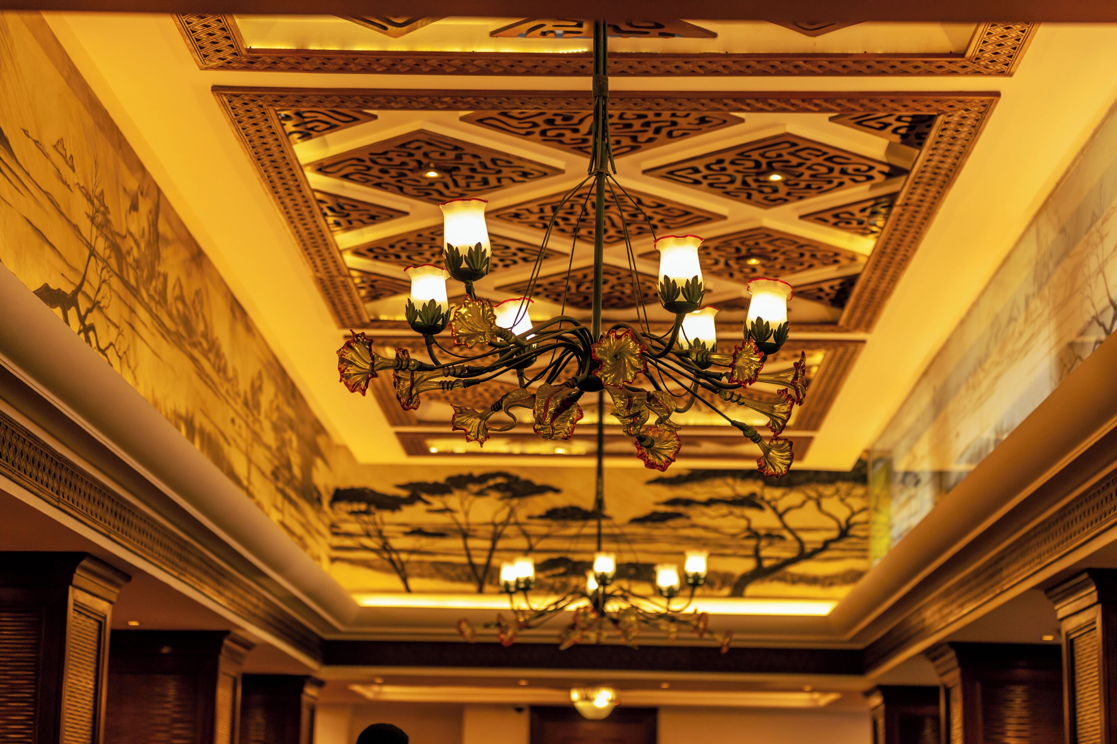 Un lustre doté de plusieurs points lumineux, un plafond orné de motifs et une fresque murale.