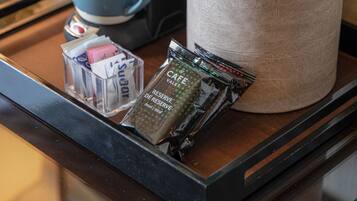 A tray with a coffee maker, a blue mug, a container of snacks, and a cylindrical container with a lid.