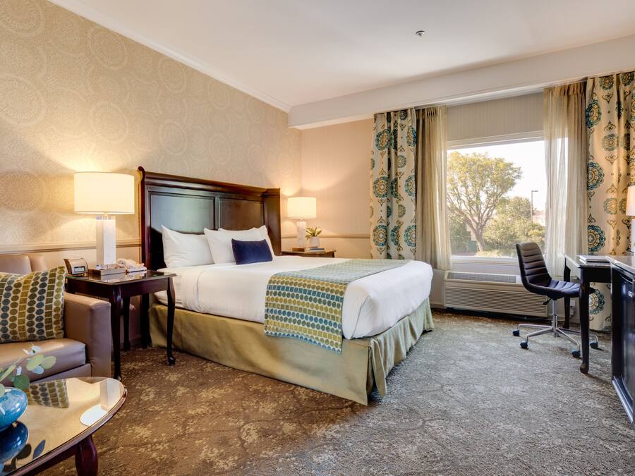 A hotel room with a bed, bedside tables, a desk, a chair, and a view of the outdoors.