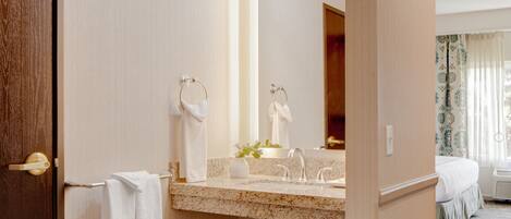 A hotel bathroom with a marble sink, a large mirror, and a wooden door.