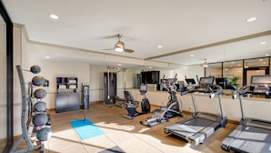 Une salle de sport équipée de tapis de course, de vélos elliptiques, d’un rameur et d’un téléviseur fixé au mur.